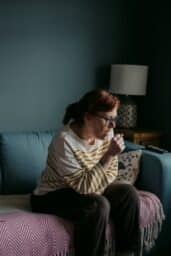A woman sitting on a couch coughing.