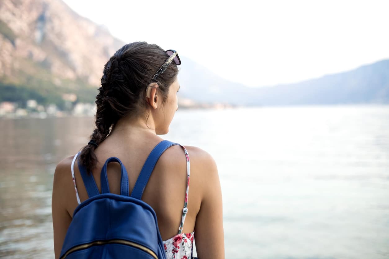 woman wearing backpack looking over water while wearing water resistant hearing aids