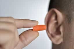 Man inserting an orange earplug into his ear.