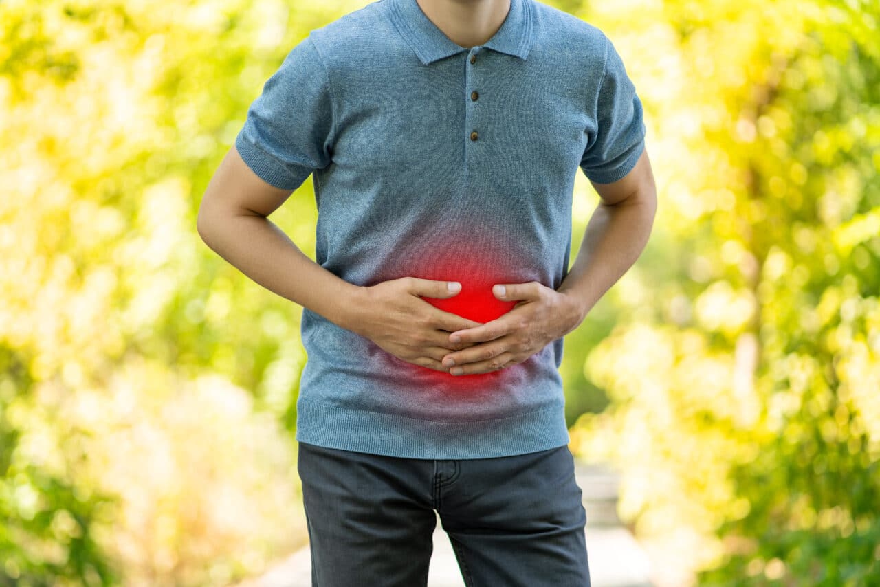 Abdominal pain when walking outdoors, man with stomach ache on nature background.