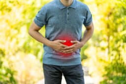 Abdominal pain when walking outdoors, man with stomach ache on nature background, health problems concept