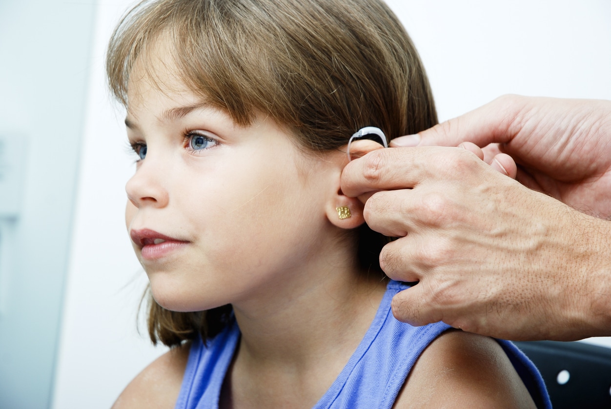 Doctor putting a hearing aid on a young girl.
