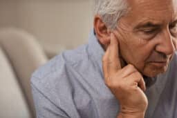 Man holding his ear worrying about hearing aids