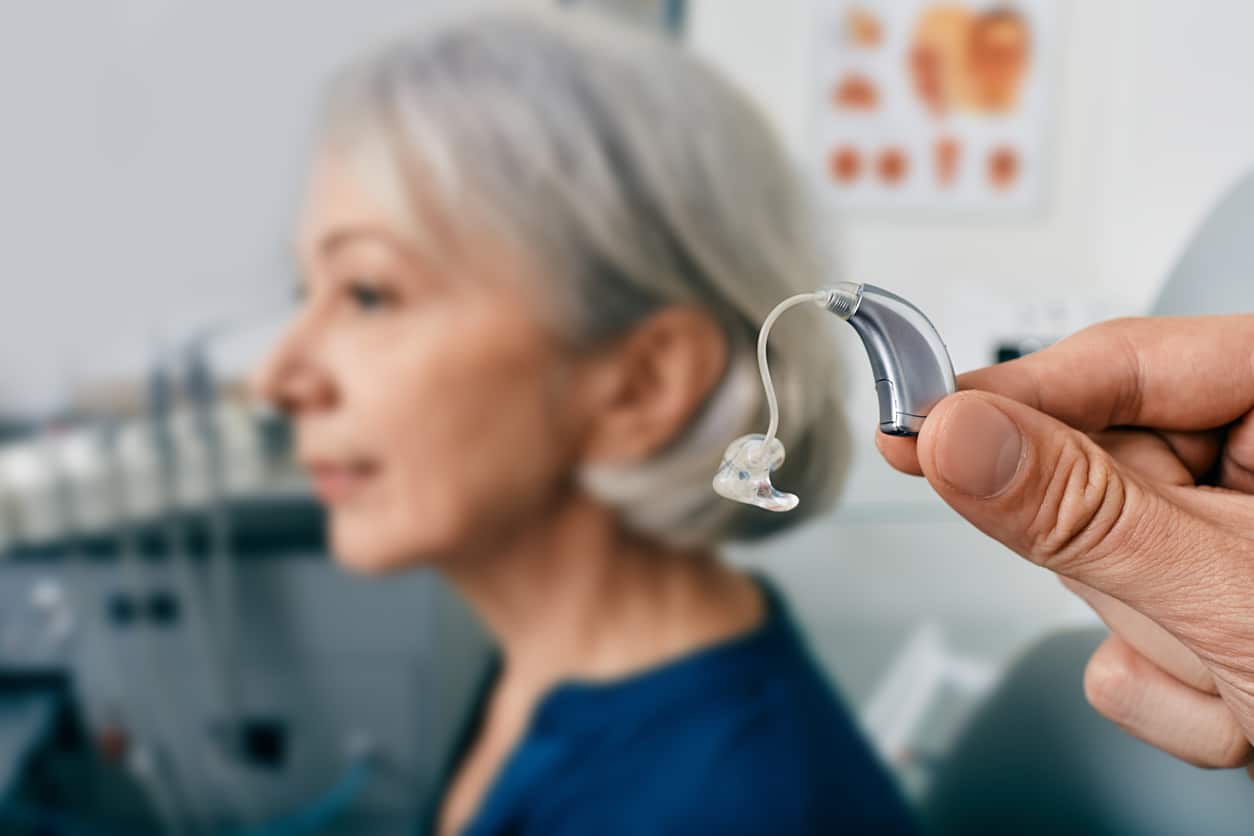 Close-up of hearing aid near senior patient's ear at audiology clinic.
