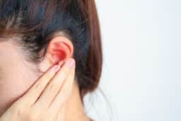 Woman holds painful spot behind ear
