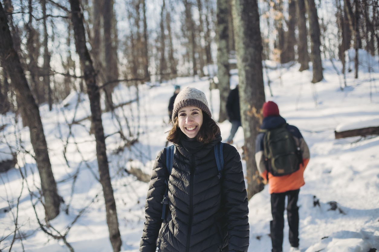 Smiling woman hiking through the snowy woods.
