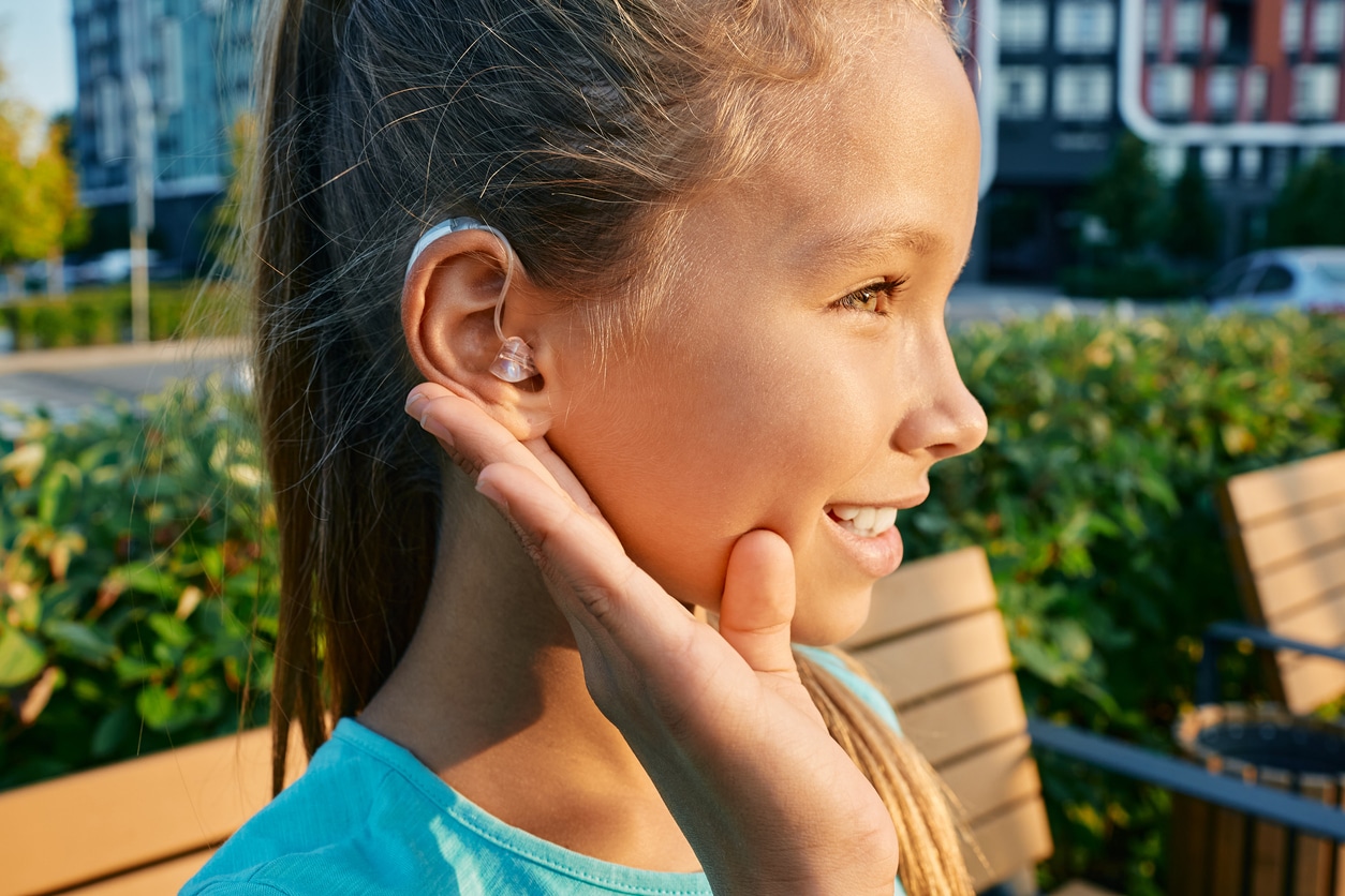 Young girl with a hearing aid sitting in the sun.