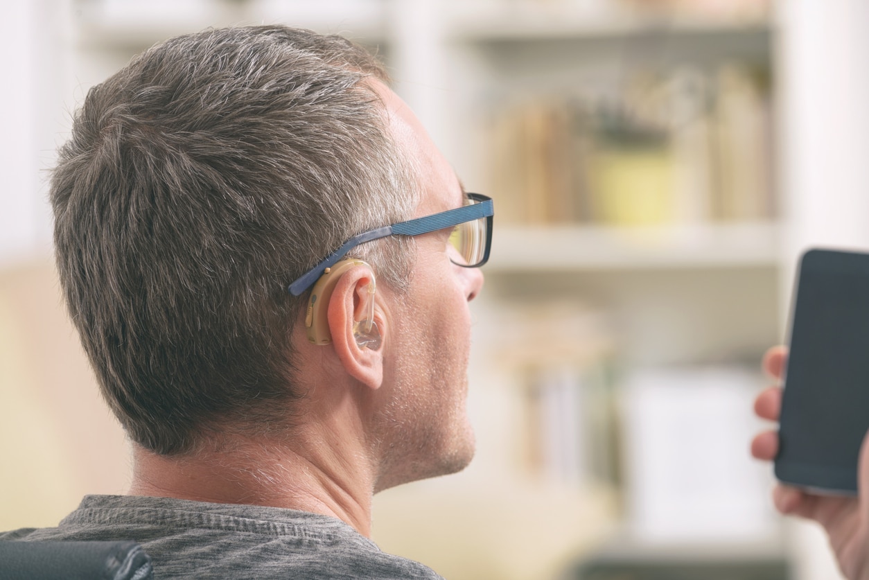 Man with a hearing aid looking at his phone.