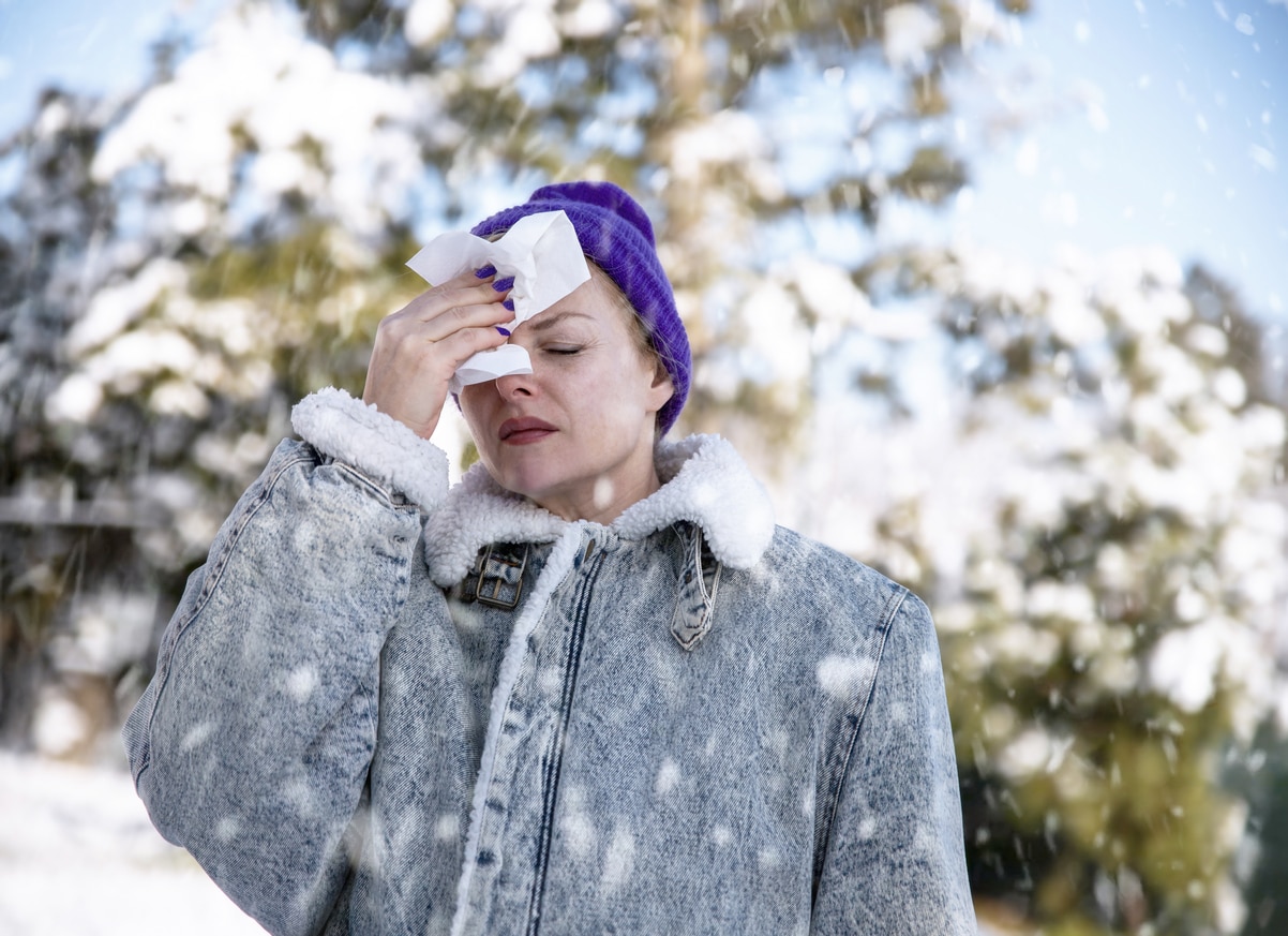 Woman standing in the snow holding a tissue to her forehead.